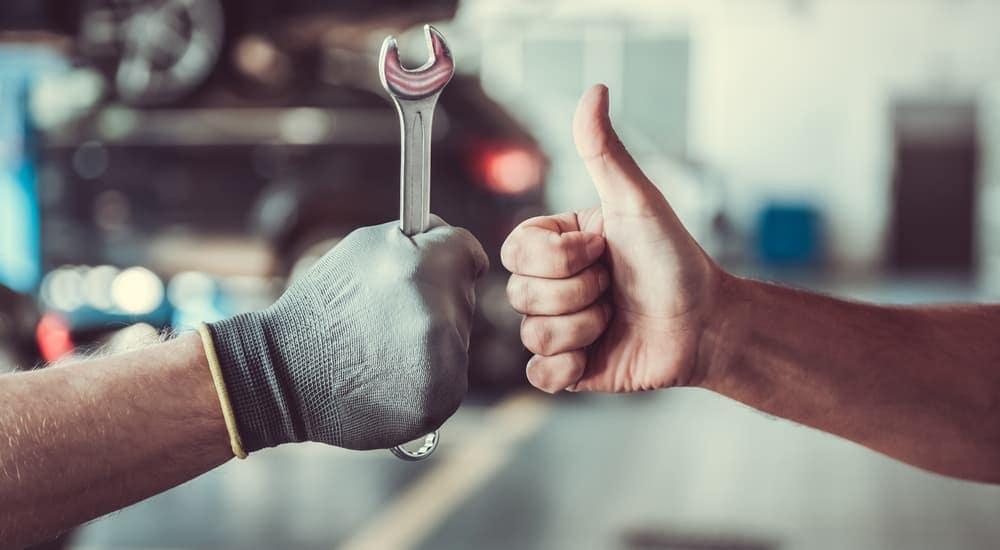 A hand is shown offering a thumbs-up next to a gloved hand holding a wrench.