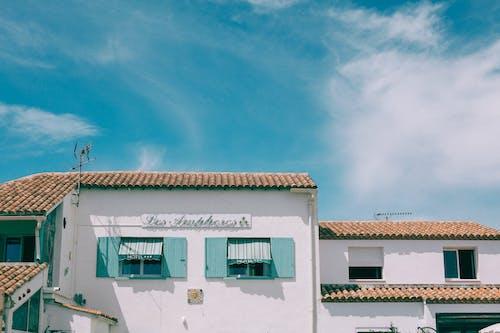 Free Exterior of cement building with wooden shutters on glass windows and red tiled roof under blue sky with clouds Stock Photo