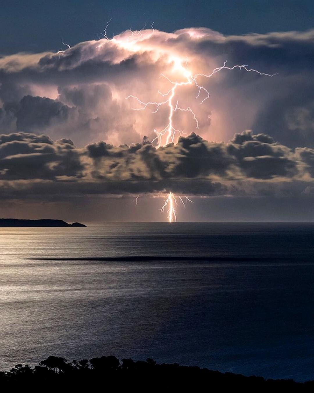 A lightning striking a cloud over water

Description automatically generated