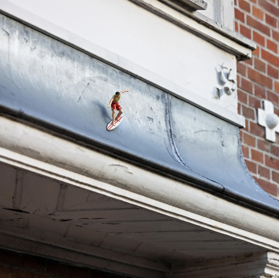 Photo of a sculpture of a miniature surfer placed on top of a ledge.