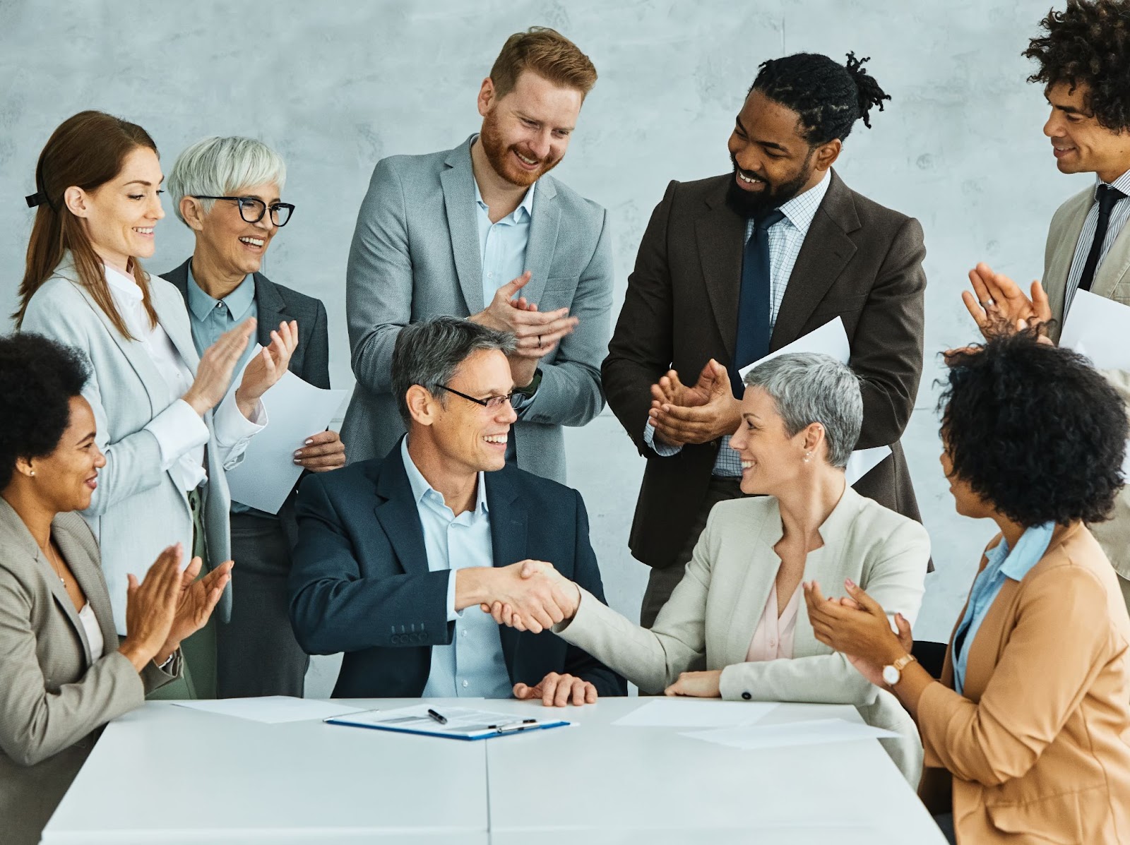 A diverse group of eight young business professionals meets in an office, exchanging handshakes to display teamwork and collaboration as they finalize a contract.