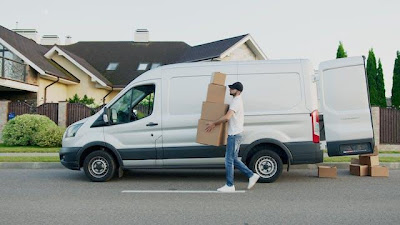 Man unloading cardboard boxes from a white van in front of a home