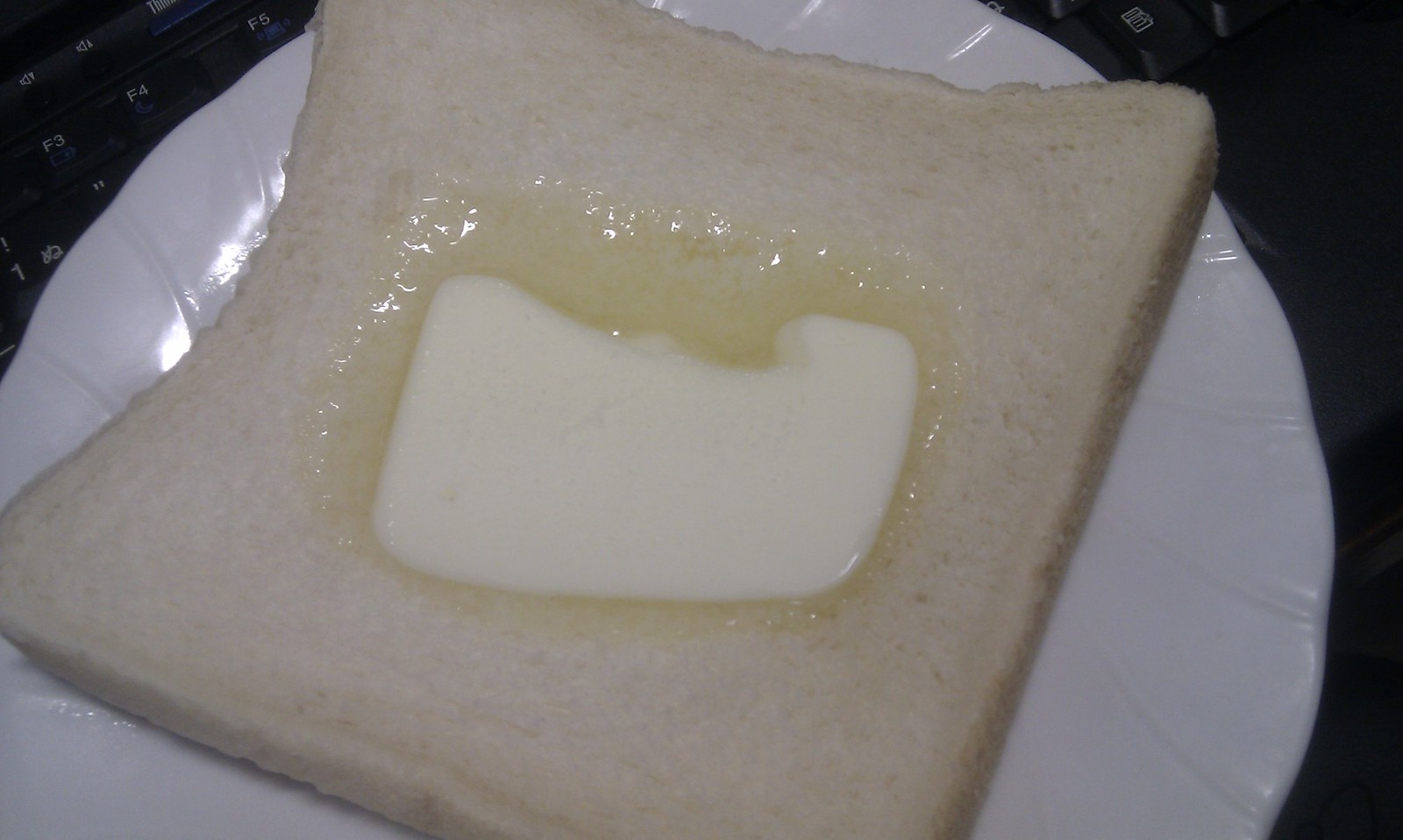 パンの上にのせられて半分溶けているバターの画像