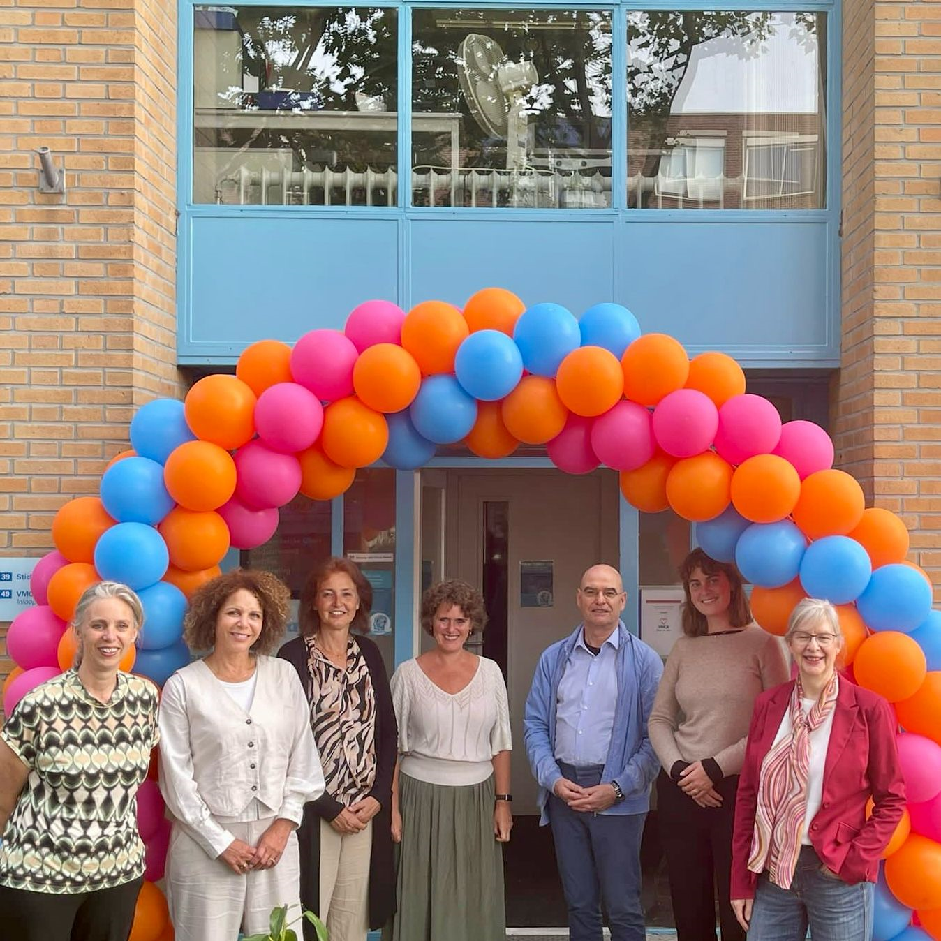 A group of people standing in front of a building with balloons

Description automatically generated