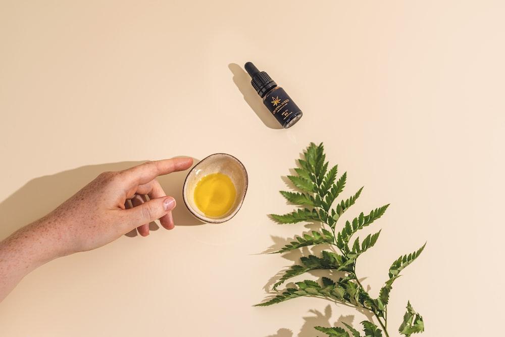 a hand holding a cup of tea next to a plant