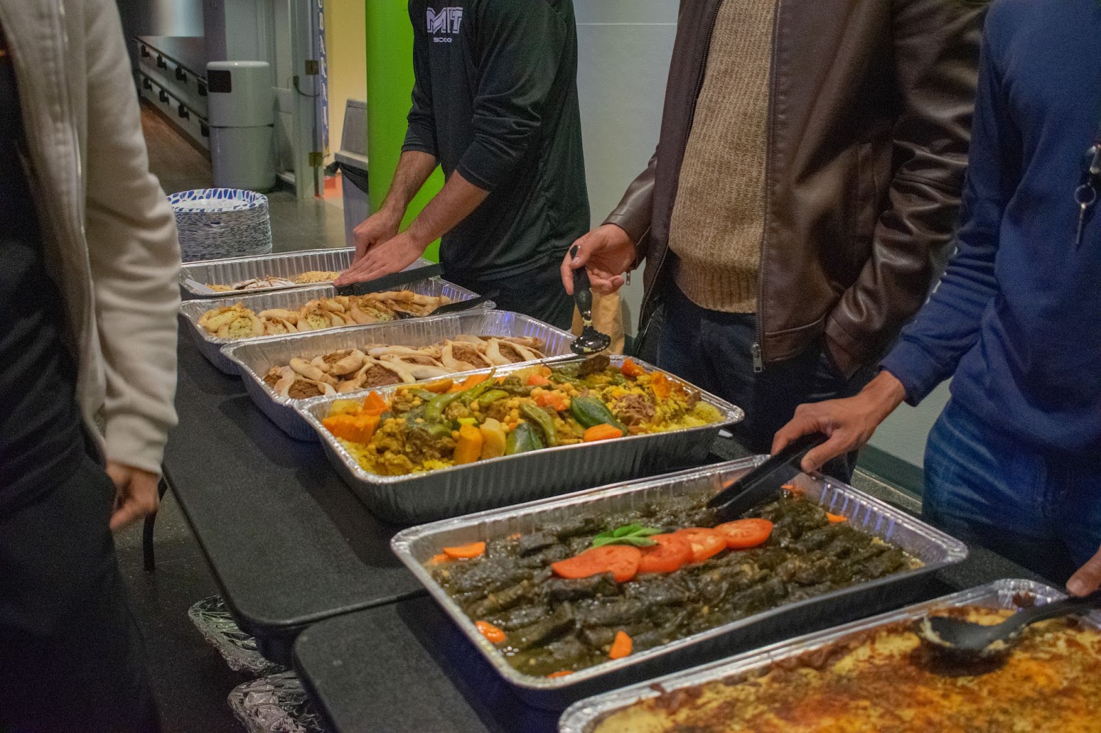 A close-up of large trays of food on a table and people serving themselves.