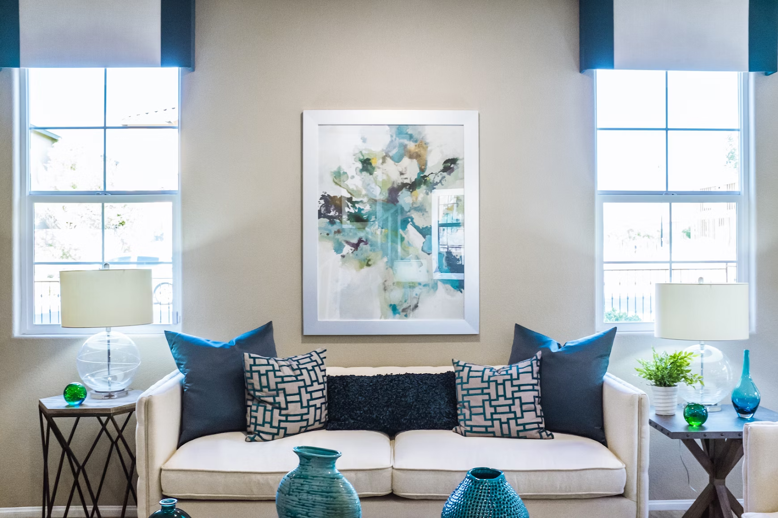 a wide shot of a living room with white and blue furniture with a framed abstract painting 