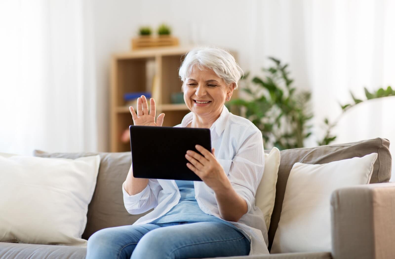 An older adult woman waving to someone she's on a video call with.