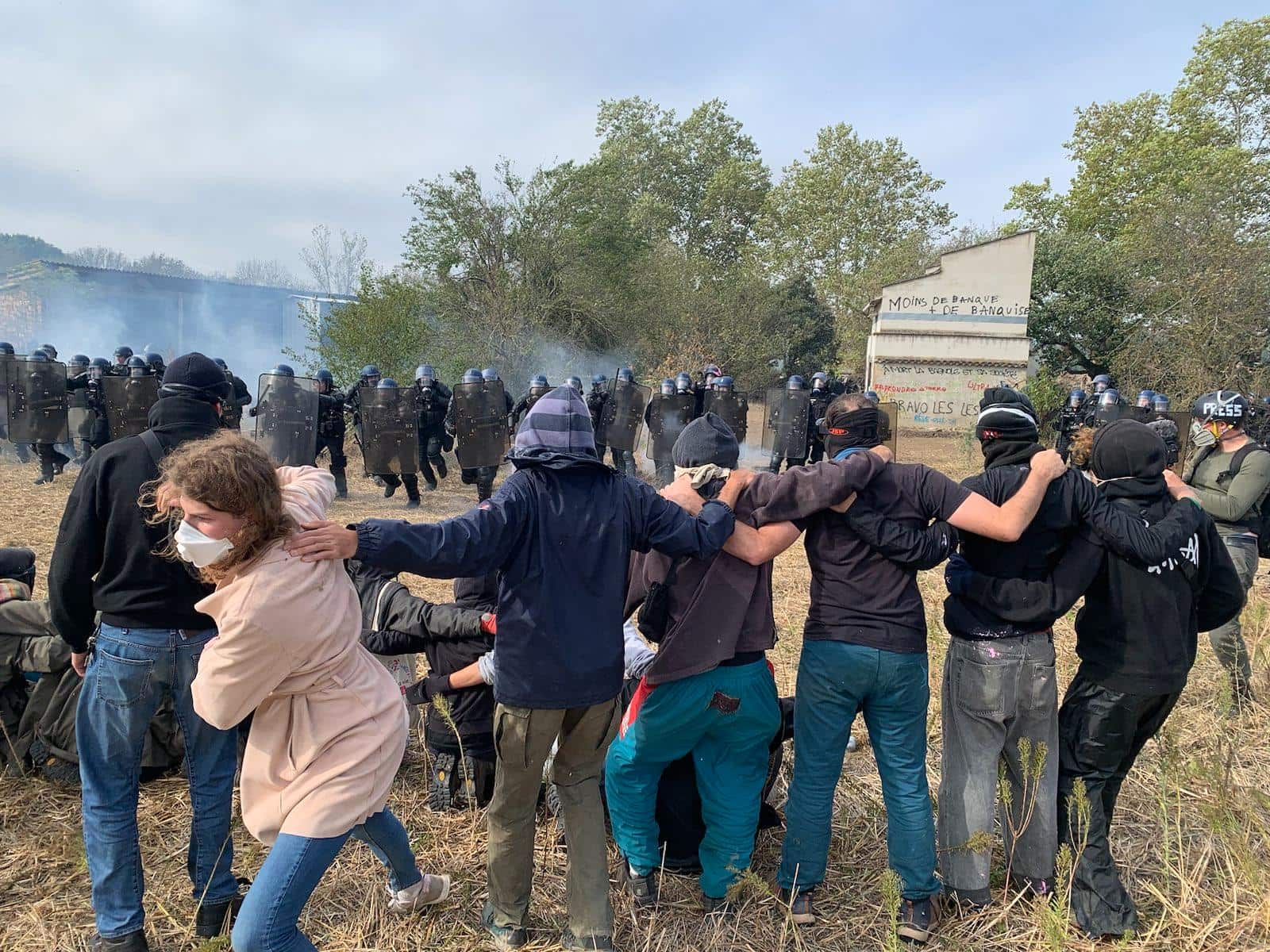Activists stand arm in arm on a field as riot police charge towards them