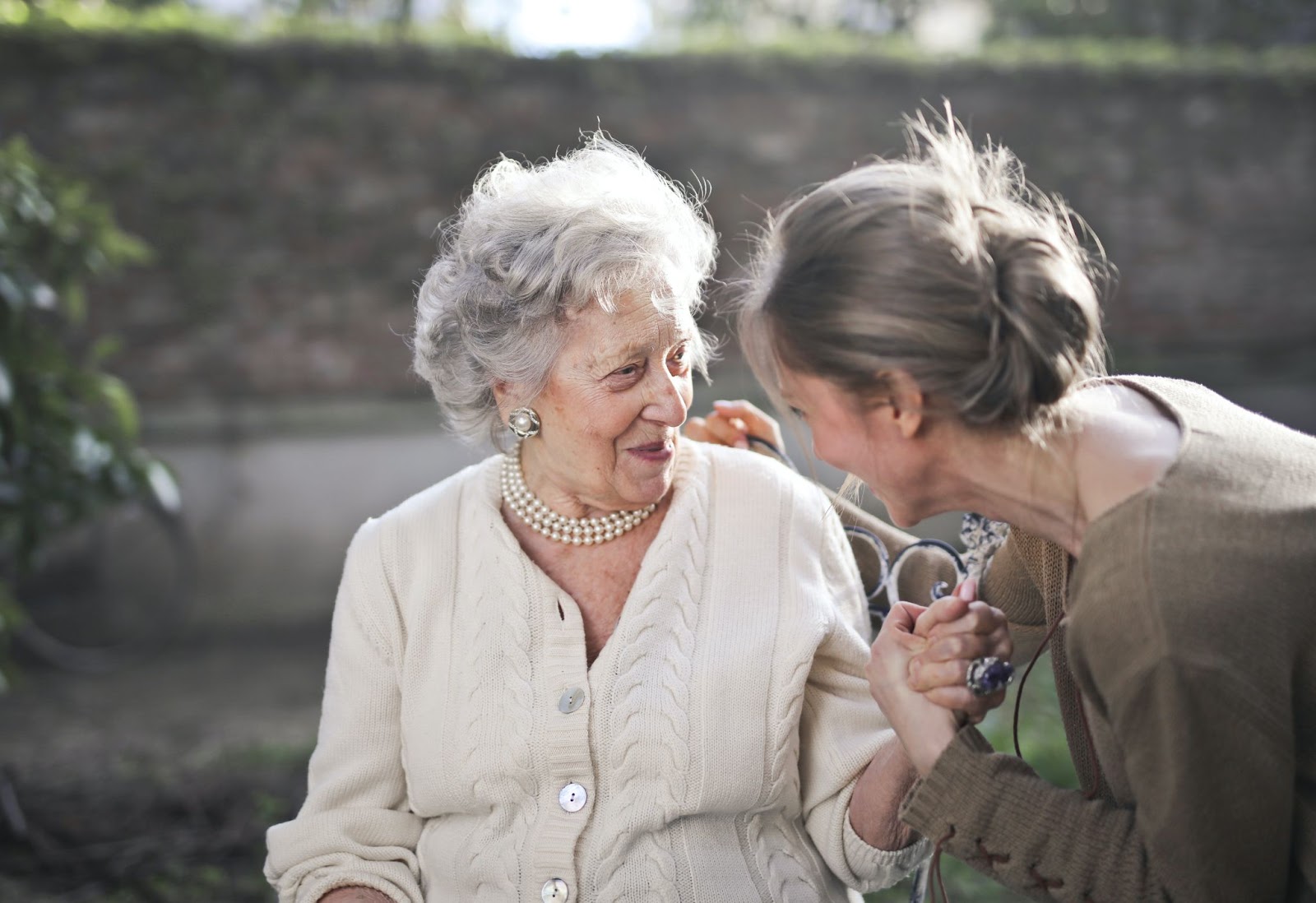 An adult laughing with her hands placed around the back of a senior citizen