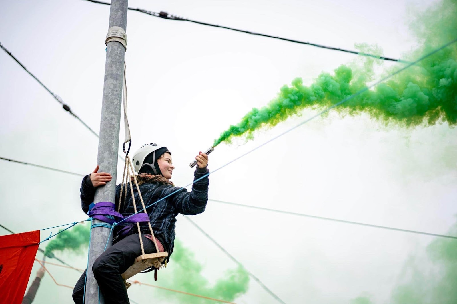 A rebel lets off a green flare while scaling a lamppost