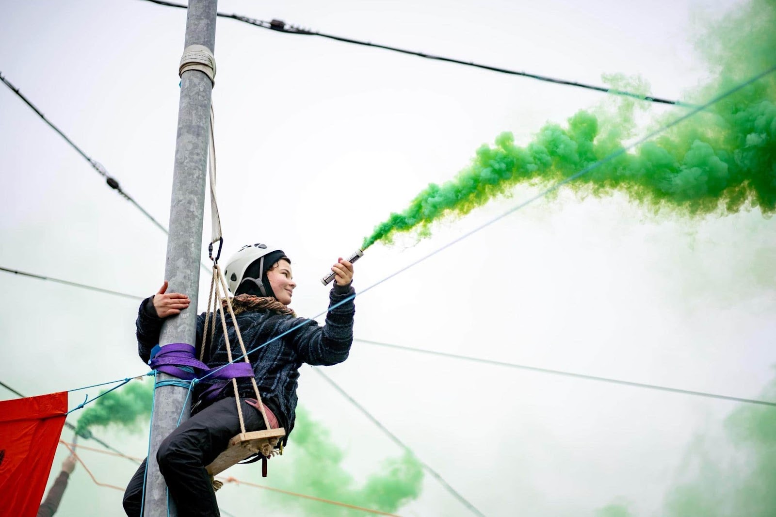 A rebel lets off a green flare while scaling a lamppost