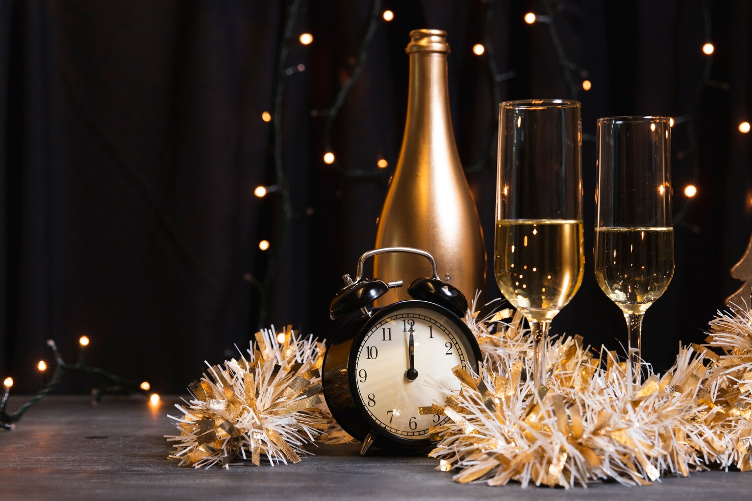 A small clock striking midnight alongside flutes of champagne to celebrate the New Year