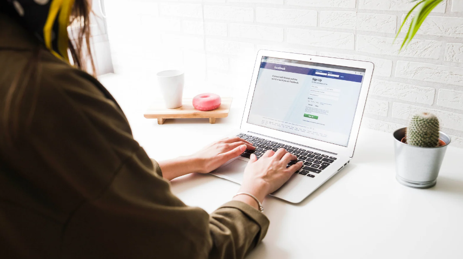 A woman using a laptop showing Facebook's login screen.