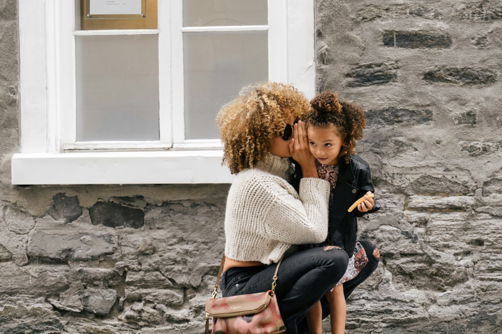 woman talking into little girl's ear with hand covering mouth