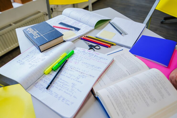 Stack of textbooks and notepads on a table, symbolising diligent A-Level English Language revision.