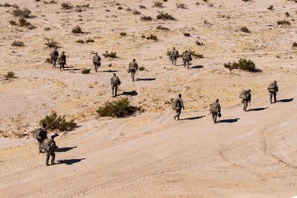 An aerial view of marines walking across a desert landscape.
