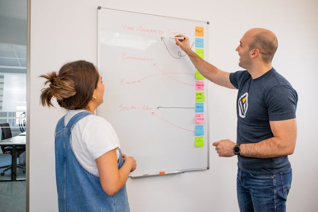 Two persons standing in front of a whiteboard, discussing and brainstorming ideas together.