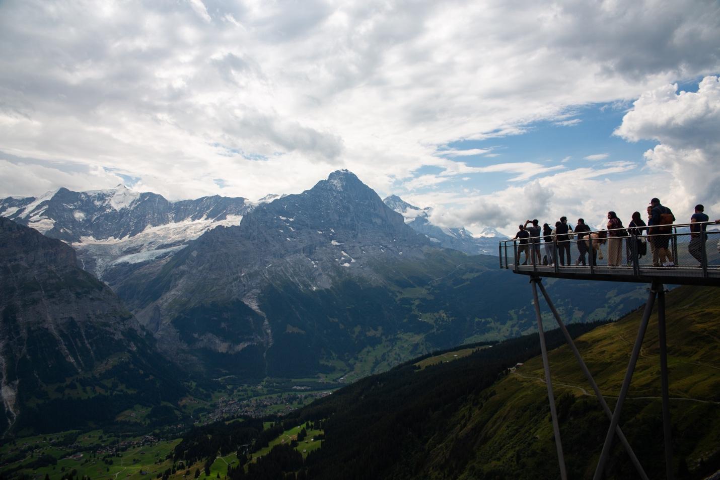 A group of people standing on a platform overlooking a valley

Description automatically generated