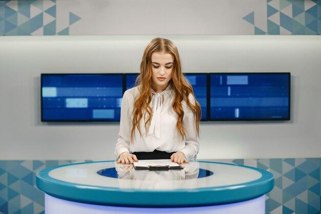 Tv present at studio preparing for new broadcasting. Smiling girl in white shirt sitting at table .