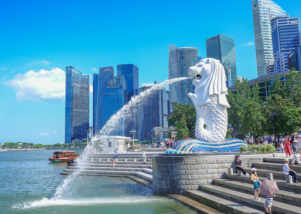 People visit the Merlion fountain in Singapore with buildings in the background.