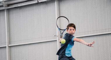ילד צעיר מניף מחבט טניס כדי לחבוט בכדור