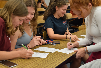 A group of girls sitting at a table writing on paper

Description automatically generated
