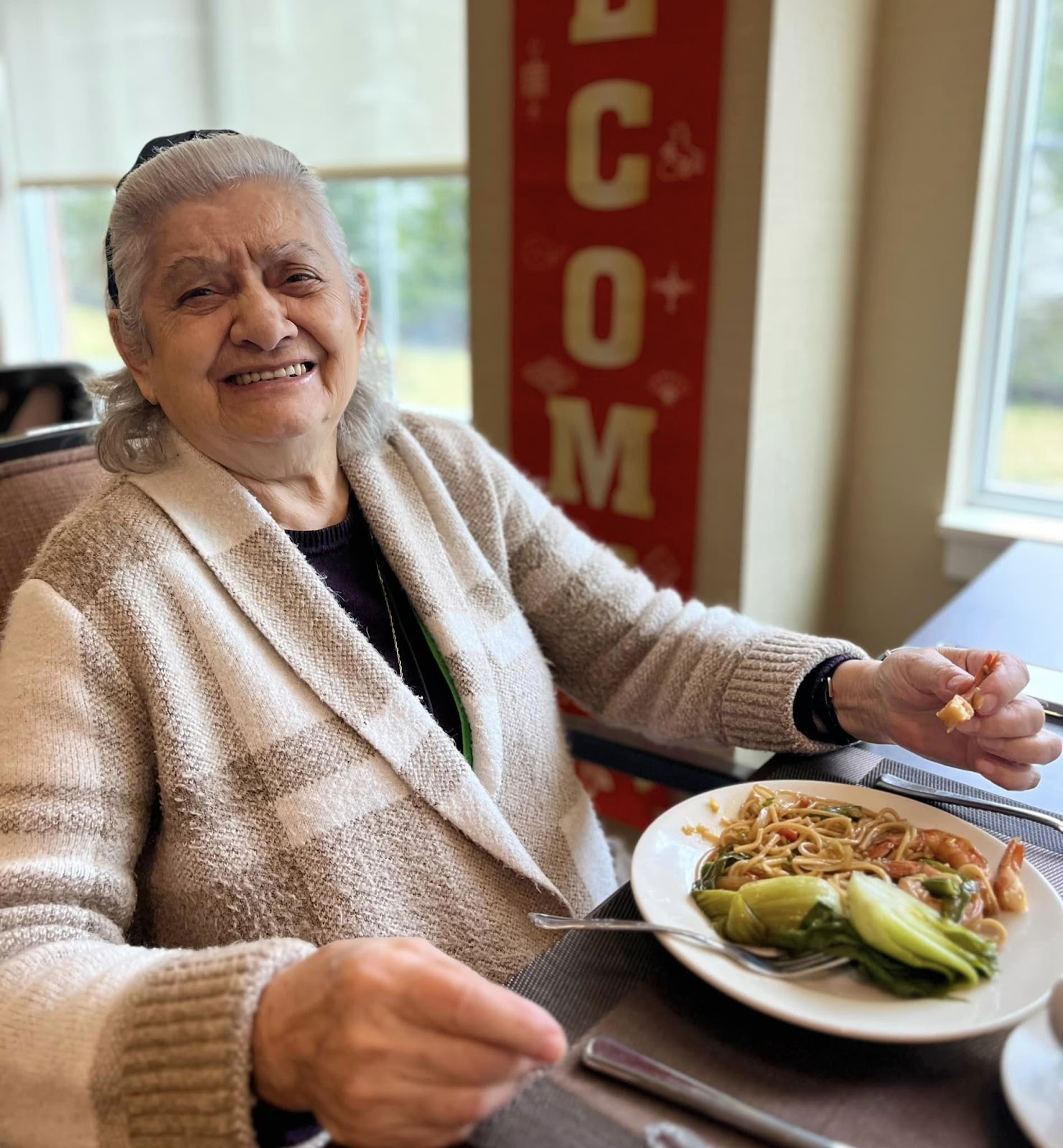 A woman in an assisted living facility smiling with a plate of pasta in front of her