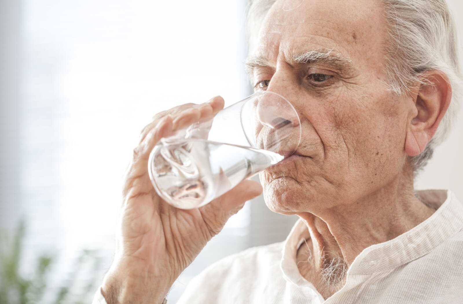 A close-up of a senior drinking a glass of water.