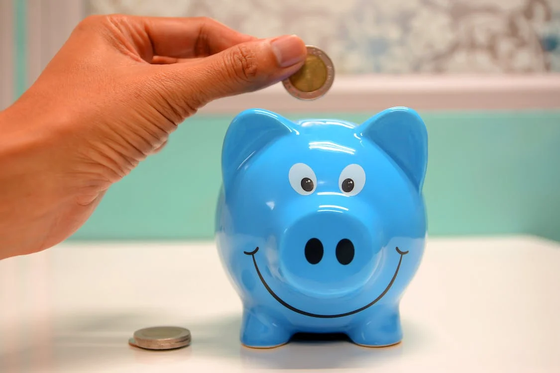 A coin being deposited in a blue piggy bank