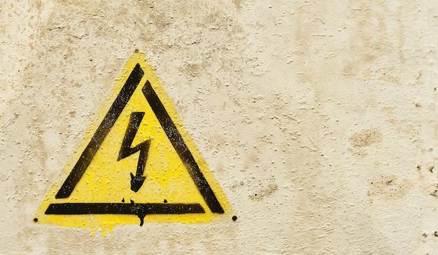 Free photo danger sign of high voltage electricity. yellow triangle hazard sign with lightning on an old gray cracked background. close-up with copy space