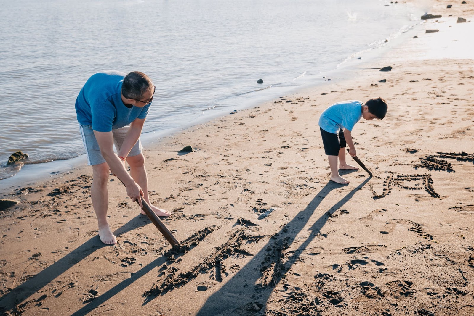 a father and son at Gyro beach in Kelowna, writing their names in the sand with sticks