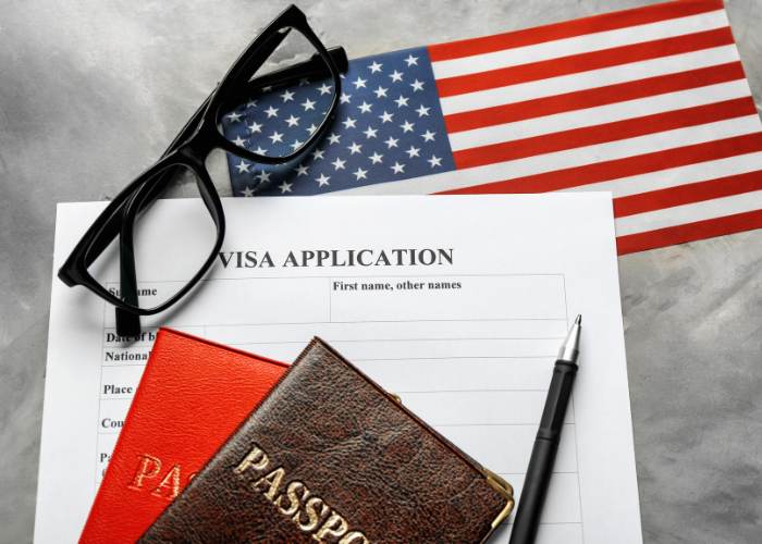 usa flag in the background with a pair of glasses, visa application form and two passport on top