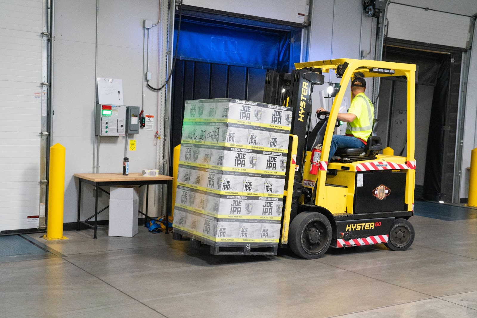 A worker in an indoor warehouse operating a forklift that uses cushion tires