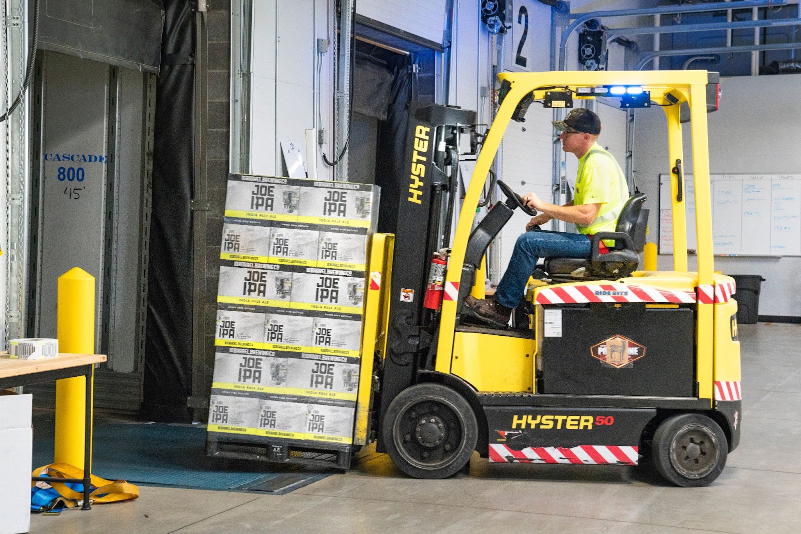 A forklift operator lifting crates of IPA beer with the tines of the forklift