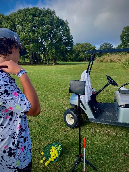 A person standing in a field with golf balls and a golf cart Description automatically generated