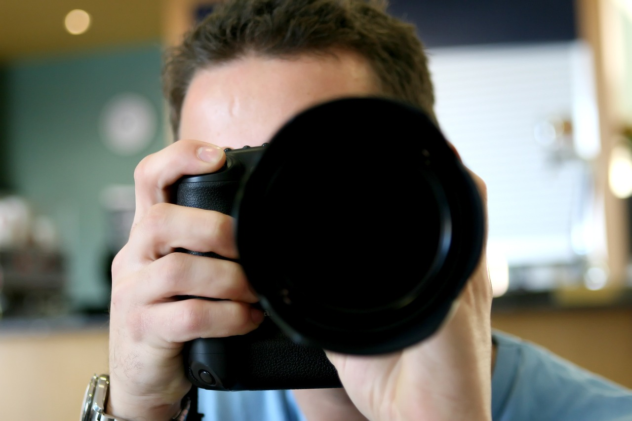 a man in a blue shirt holding up a black camera and aiming it at the viewer