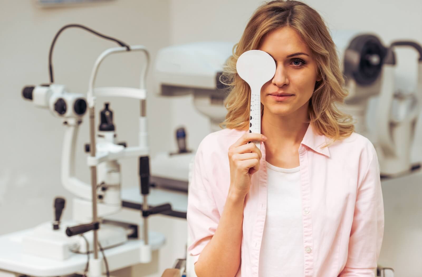 A woman blocking her right eye with a white occluder as a part of her visual acuity test.
