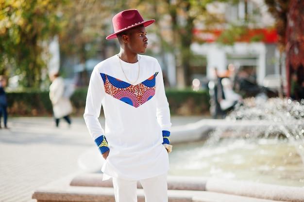 Stylish trendy afro france man in red hat and white outfit posed at autumn day Black african model guy