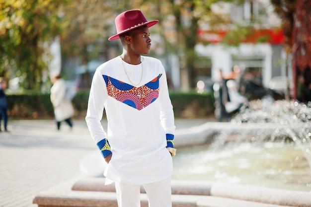 Stylish trendy afro france man in red hat and white outfit posed at autumn day Black african model guy
