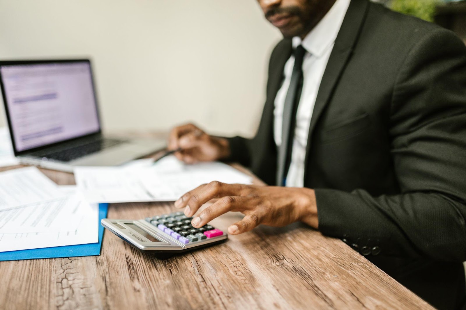 A man in a black suit typing numbers in to a calculator