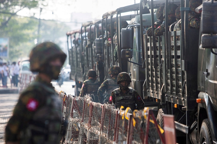 Soldiers stand next to military vehicles.