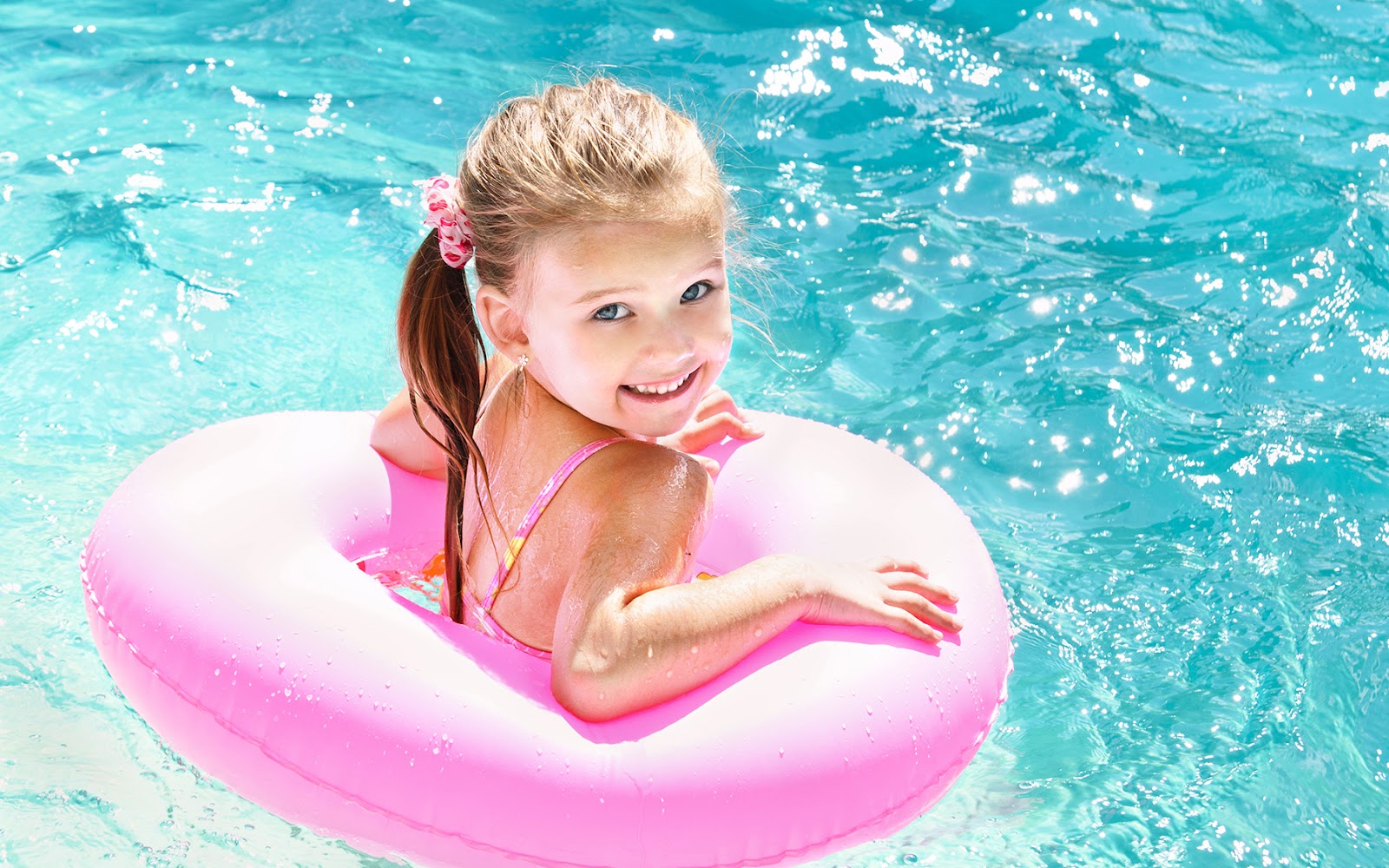 smiling little girl swimming in pool in pink ring float