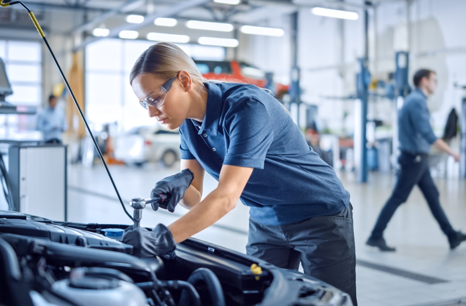 A female mechanic working on a car and wearing prescription safety glasses