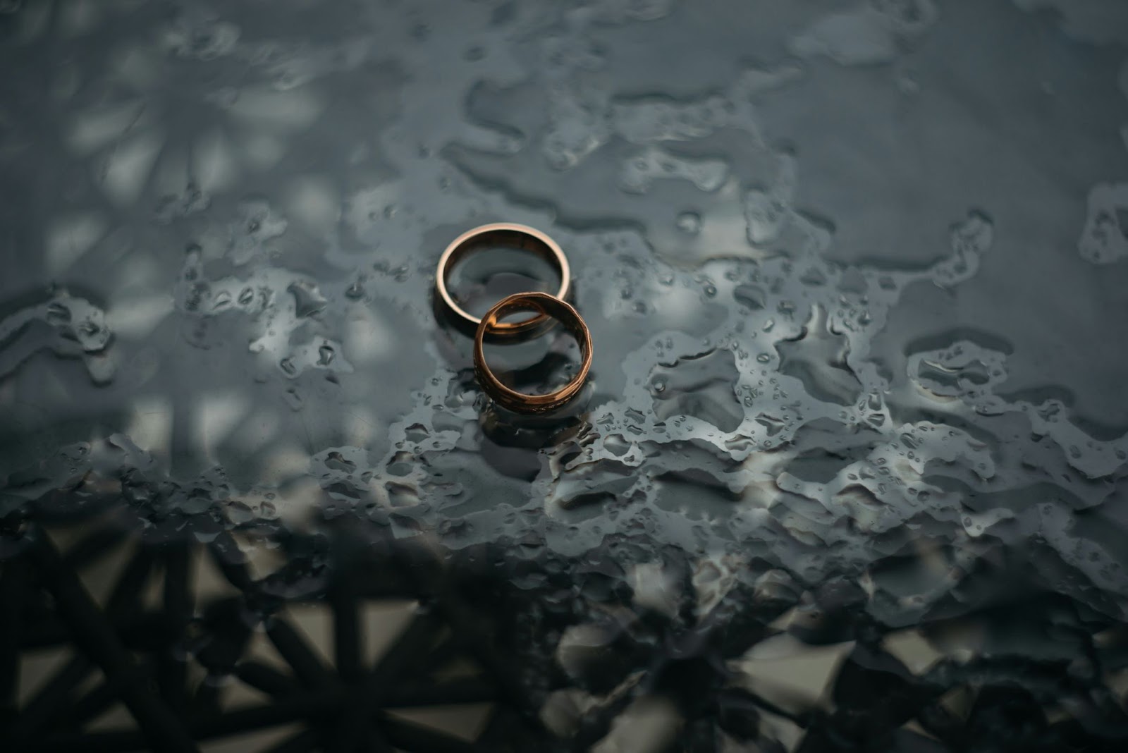 Matching gold wedding bands on glass table top.