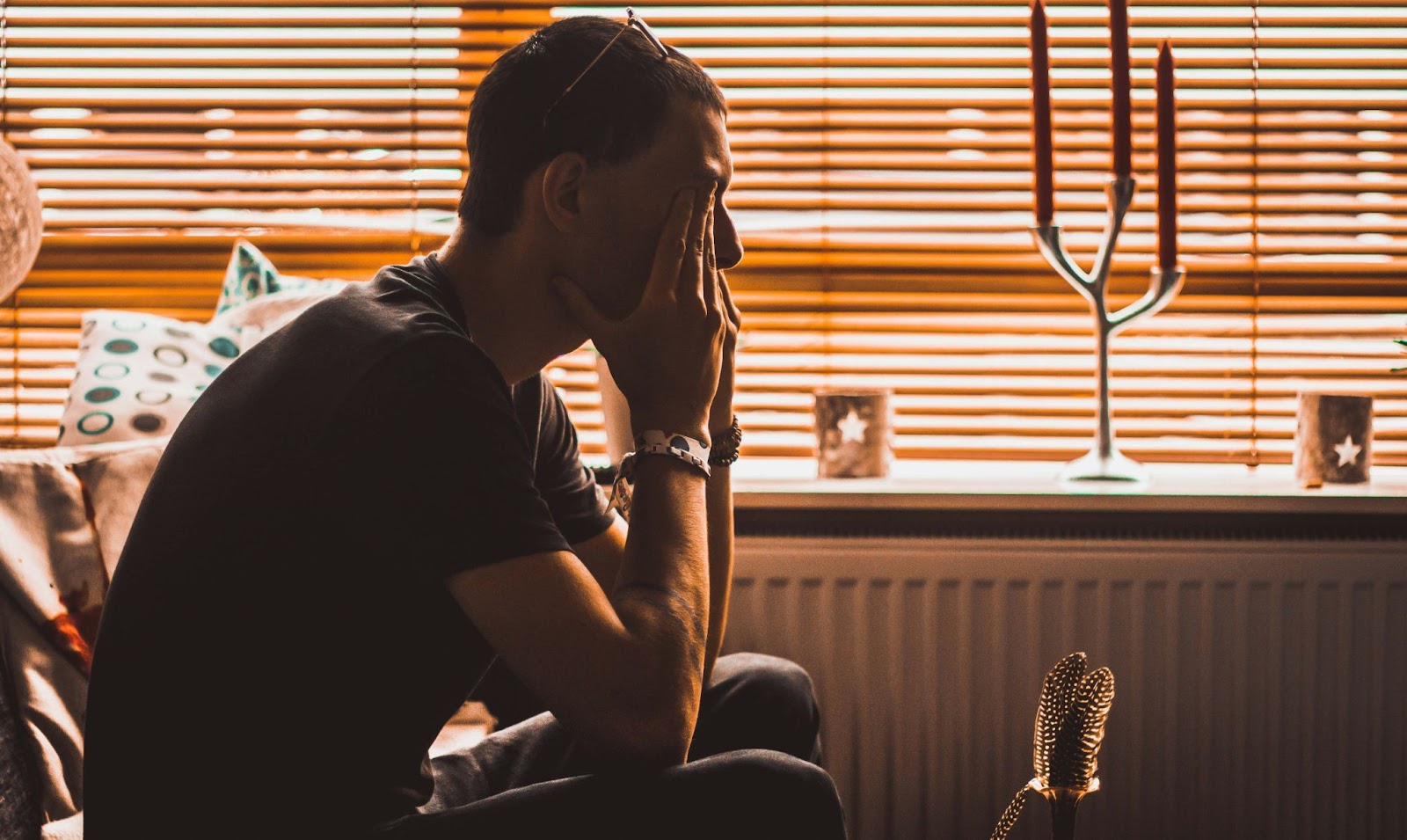 a man sitting on a sofa, with his 2 hands on his face, looks concerned