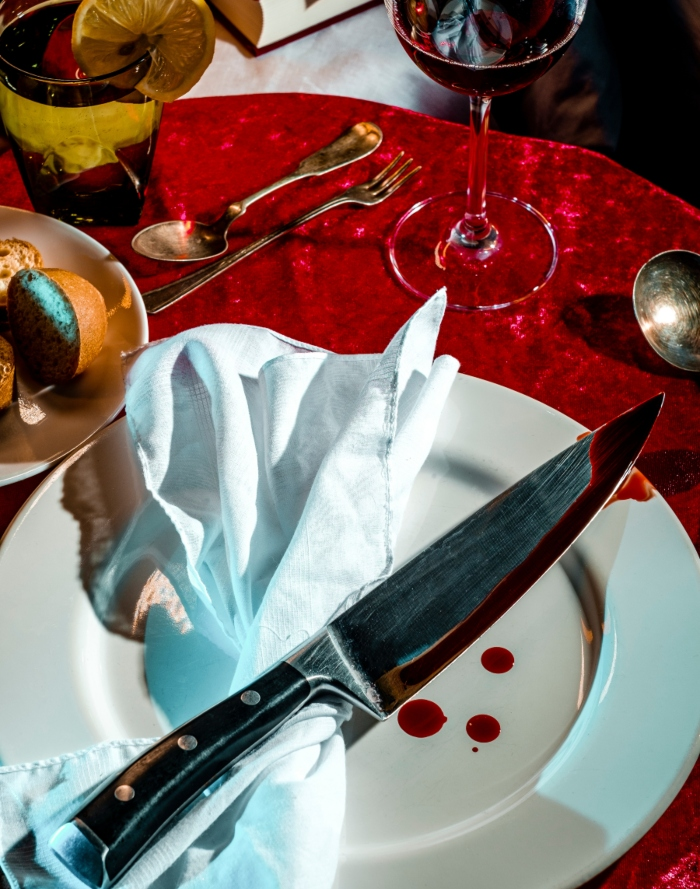 A knife covered in blood on a plate with napkin on the Murder Mystery Dinner table. 