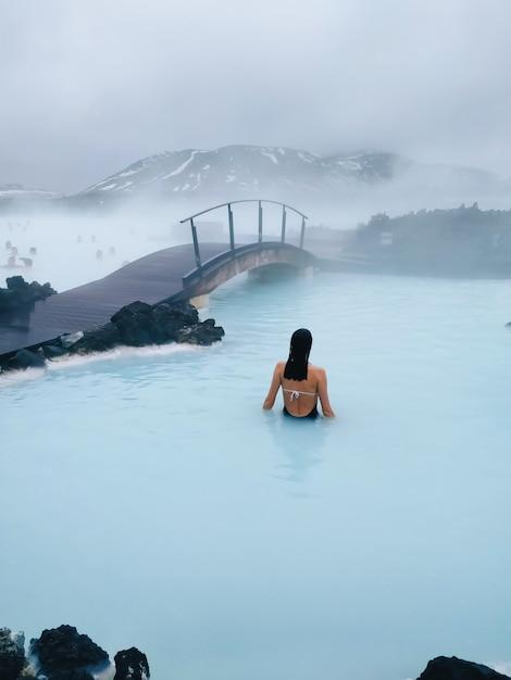 Free photo vertical shot of a female swimming in a hot pool near the bridge
