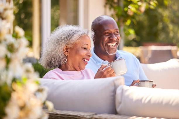 Retired Couple Sitting Outdoors At Home Having Morning Coffee Together Retired Couple Sitting Outdoors At Home Having Morning Coffee Together black lovers stock pictures, royalty-free photos & images