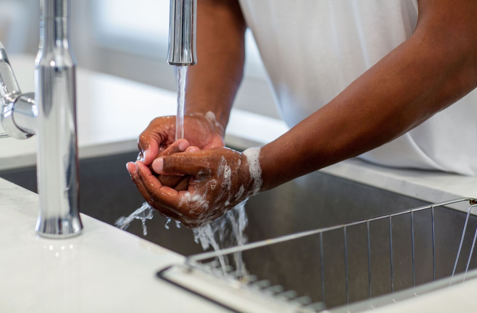 A close-up of a person washing their hands at a kitchen sink with soap and water.
